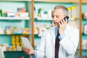 Apotheker schaut auf Rezept und telefoniert mit Arzt