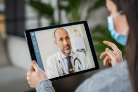 Patientin mit Maske konsultiert Arzt über Video