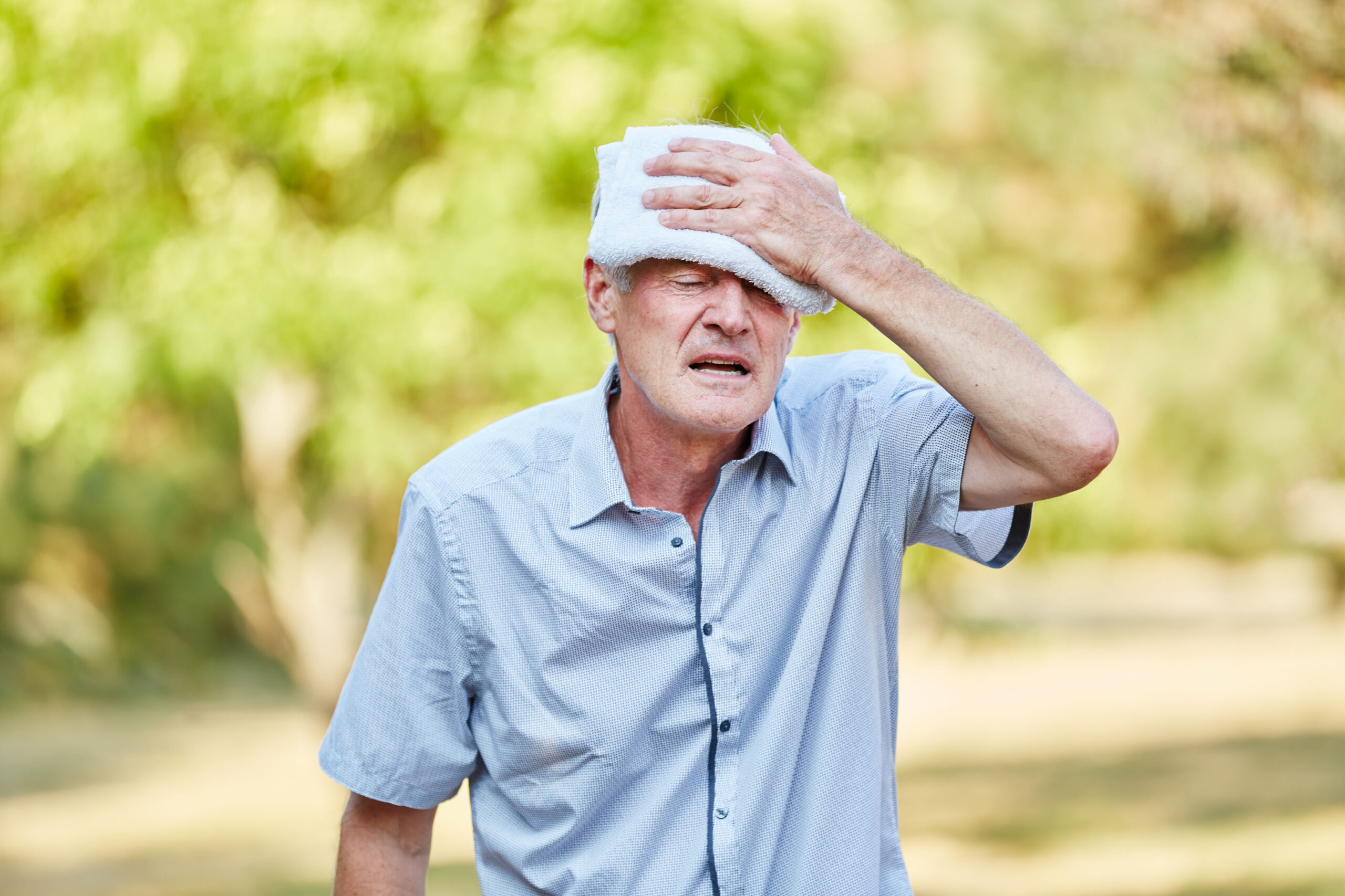 Senior kühlt sich mit Waschlappen den Kopf